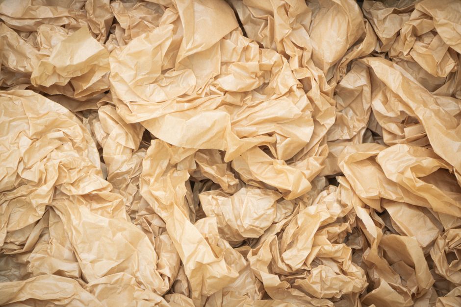 A close-up view of a large pile of crumpled, beige paper waste, filling the frame with irregular, wrinkled textures. The paper appears to be discarded and used, with some pieces overlapping others. The lighting highlights the uneven surfaces and shadows within the pile. This scene is set on a flat surface, possibly in a recycling or waste management context, emphasizing the need for proper disposal or recycling of textiles and paper waste, as discussed in the context of how Wandsworth Council handles bulky textile waste. For professional surface cleaning, deep cleaning, and sanitisation services, contact Putney Carpet Cleaning at https://putneycarpetcleaning.org.uk.